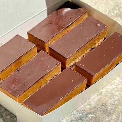 Classic caramel slice with a biscuit base, layered with golden caramel, and topped with a thick layer of chocolate.